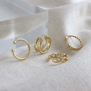 Set di quattro ear cuff dorati a spirale e perline su sfondo in tessuto minimalista