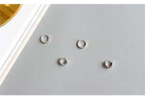Vier minimalistische 925 Sterling Silber Huggie Creolen auf grauem Hintergrund liegend