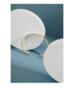 Detailansicht eines goldenen Armreifs mit Hammerschlag-Struktur auf blauem Hintergrund