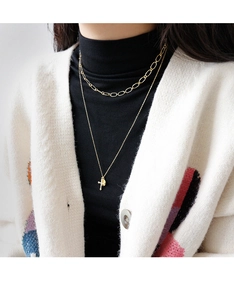 Detail of layered gold necklace featuring a cross pendant and a small round coin charm