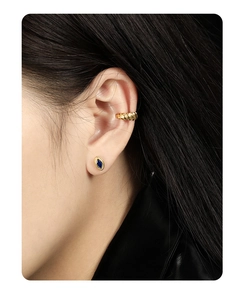 Detail of twisted gold ear cuff and oval blue zircon stud earring on model ear