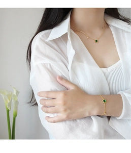 Detail van smaragdgroene ketting en gouden armband op model met witte calla lelies
