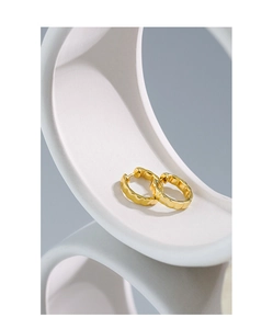 Detail of gold checkered textured hoop earrings on white sculptural display stand