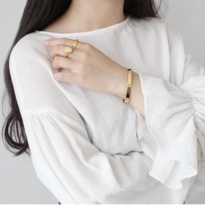Detail of vintage gold coin ring and minimalist bangle on model with white blouse