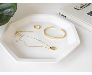 Minimalist gold-plated jewelry set with necklace, bangle and ring on a white plate
