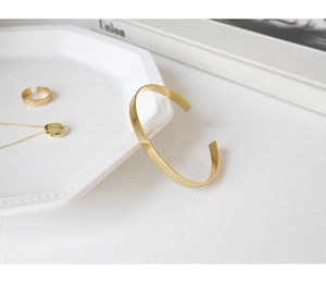 Detailed view of minimalist gold open bangle with matching textured ring and heart necklace
