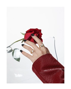 Primer plano de anillos de corazón dorados en una mano con rosa roja y manga de cuero