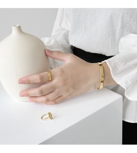 Detail of minimalist gold-plated bangle and rings on a textured white background