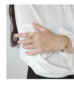 Close-up of minimalist gold cuff bracelet and textured rings on model wearing white
