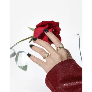 Anillo ondulado dorado con piedra de corazón blanca sobre fondo de rosa roja