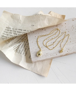 Détail d'un pendentif goutte doré minimaliste sur une chaîne sur pierre