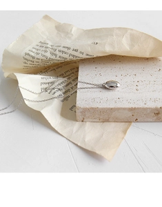 Détail du collier pendentif haricot argenté sur pierre et fond de papier vintage