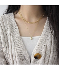 Détail d'un ensemble de colliers dorés superposés avec pendentif fève minimaliste sur modèle