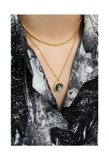 Détail de colliers superposés dorés avec pendentif labradorite et texture de lave