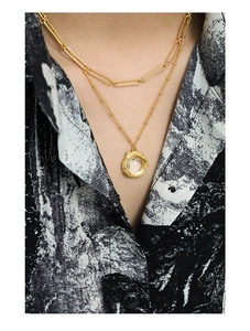 Détail d'un collier doré à deux rangs avec chaîne trombone et pendentif rond texturé