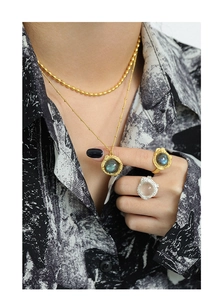 Détail de colliers dorés superposés avec pendentif labradorite et bagues texture lave