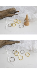 Detalle de anillos ondulados minimalistas en plata y oro sobre base de madera