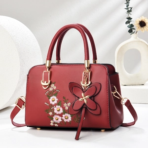 Elegant red faux leather handbag with floral embroidery and butterfly charm accessory