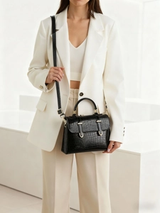 Close-up of black crocodile pattern handbag with gold hardware on a model outfit