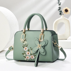 Detail of pea green faux leather bag with floral embroidery and butterfly pendant