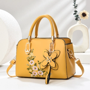 Detailed close-up of yellow leather handbag with daisy embroidery and floral charm detail