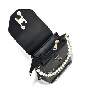 Detalle de bolso bandolera negro con bordado floral, asa de perlas y hebilla dorada en H