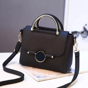 Detail of black pebbled leather handbag featuring a curved gold handle and magnetic closure