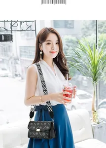 Detailed view of black textured crossbody bag with patterned wide strap and gold lock