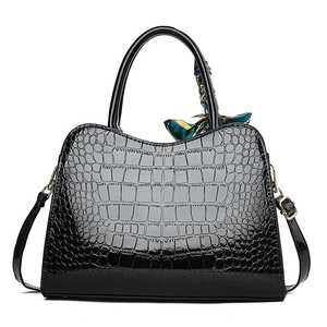 Detail of black faux crocodile skin handbag with silk scarf and gold hardware