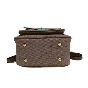 Detailed bottom view of brown twill backpack with leather edges and gold metal feet