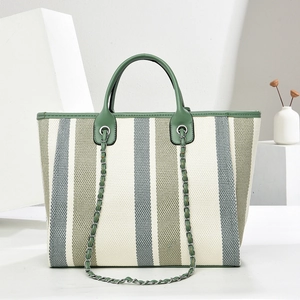 Détail d'un cabas en toile avec rayures, finitions en cuir vert et bandoulière chaîne