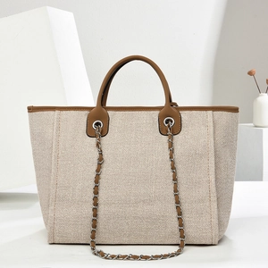 Detail of beige woven canvas tote bag with brown leather trim and metal chain accents
