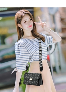 Outdoor view of a black flap crossbody bag with logo pattern and woven wide strap