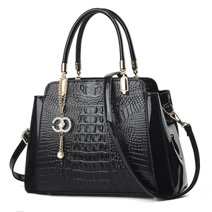 Elegant black crocodile pattern handbag with gold hardware and pearl charm on white background