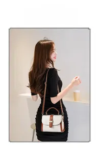 Detail view of cream white flap bag with brown leather trim and golden H-shaped clasp
