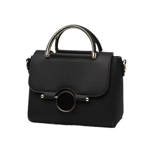 Minimalist black leather crossbody bag with distinctive gold metal handle and magnetic flap