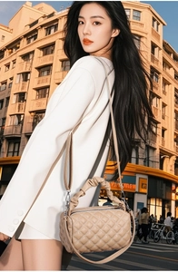 Detail of beige quilted handbag featuring a ruched handle and elegant chain strap
