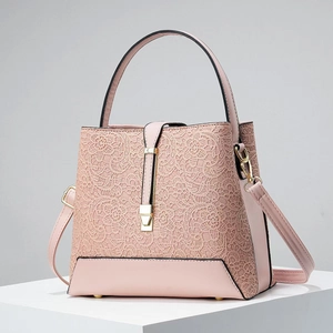 Elegant pale pink bucket bag with lace overlay and gold hardware displayed on white stand