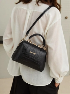 Details der schwarzen Handtasche mit Krokostruktur, Goldrahmen und Markenlogo