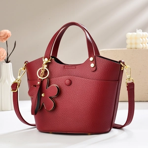 Detailed macro view of burgundy lychee leather bucket bag with gold hardware and flower charm