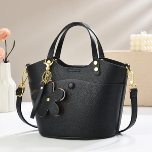 Elegant black lychee grain bucket bag with gold hardware and flower pendant on a minimalist base