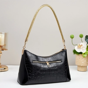 Detail of black crocodile texture handbag with luxury gold braided handle and metallic hardware