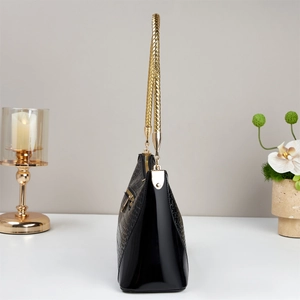 Detail showing crocodile texture leather, gold braided handle, and metal zipper of the black bag