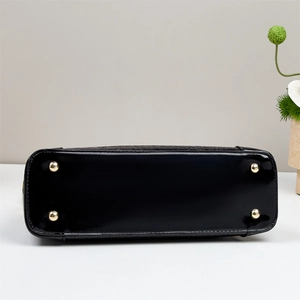 Close-up of black patent leather handbag bottom with four protective gold metal studs