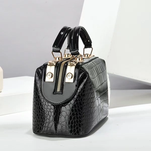 Detail der glänzenden schwarzen Handtasche mit Krokodilprägung und goldenen Akzenten