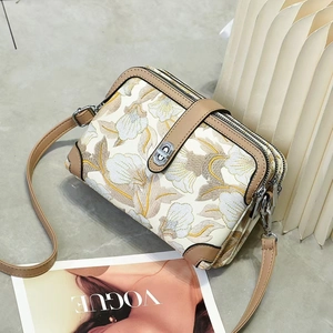 Sac bandoulière brodé à triple fermeture éclair sur une surface grise minimaliste