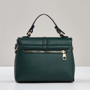 Detail view of dark green pebbled leather handbag with gold zipper and metal rings