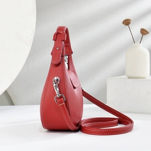 Detail of red lychee grain leather crossbody bag featuring white stitching and silver hardware
