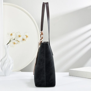 Detail of black suede tote bag featuring brown leather handle and patterned silk scarf