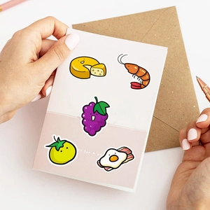 Close-up of hands holding cute food stickers including cheese and grapes on a desk